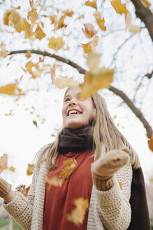 Ein Mädchen im Teenageralter wirft im Freien Herbstblätter in die Luft. - MINF03431