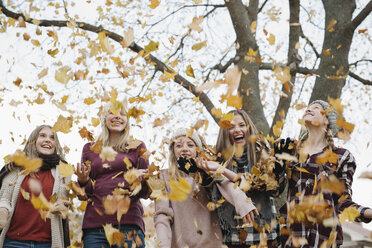 A group of five teenage girls outdoors in woolly hats and scarves throwing autumn leaves in the air. - MINF03434