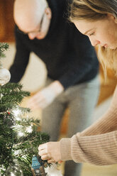 Ein Vater und seine Tochter schmücken einen Weihnachtsbaum. - MINF03437