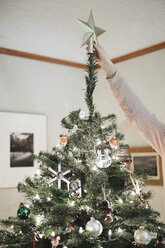 Eine Person, die einen Weihnachtsbaum zu Hause schmückt. - MINF03439