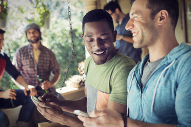 Eine Gruppe von Freunden, Männer und Frauen auf einer Hausparty, zwei Männer schauen auf ihre Smartphones. - MINF03448