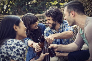 Eine Gruppe von Freunden liegt in einer großen Hängematte im Garten und trinkt ein Bier. - MINF03462