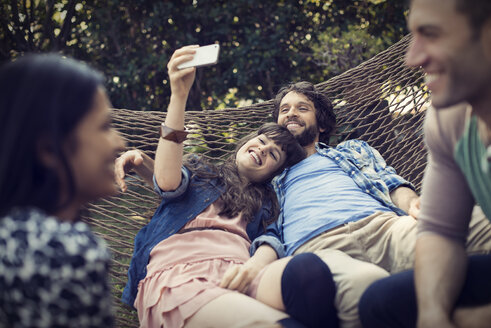 Eine Gruppe von Freunden, die in einer großen Hängematte im Garten liegen, ein Bier trinken und ein Selfie machen. - MINF03465