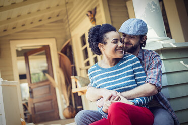 Ein Paar, ein Mann und eine Frau, sitzen auf den Stufen der Veranda und lachen. - MINF03467