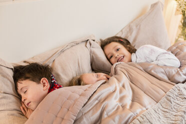 Three children lying in a bed under the covers. - MINF03481