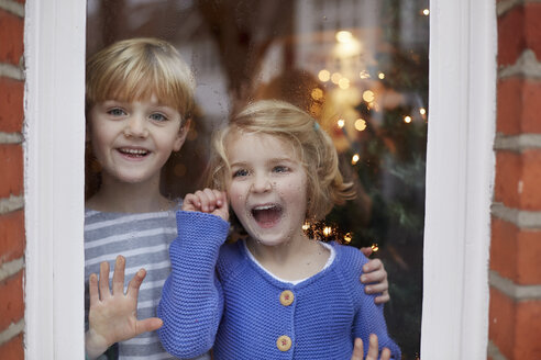 Zwei Kinder, ein Junge und ein Mädchen, schauen mit aufgeregter Miene aus dem Fenster ihres Zuhauses. - MINF03486