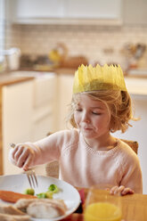 Ein junges Mädchen, das einen Partyhut trägt, sitzt an einem Tisch und isst. - MINF03488