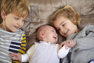 Drei Kinder liegen auf einem Bett, ein Junge und ein Mädchen mit einem Baby zwischen ihnen. - MINF03496