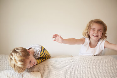 Zwei Kinder spielen hinter einem Sofa, ein Junge und ein Mädchen lachen. - MINF03497