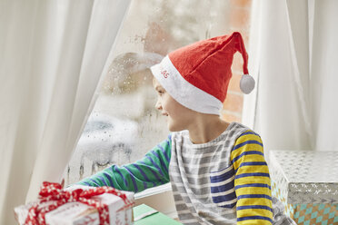 Weihnachtsmorgen bei einer Familie: Ein Junge mit Weihnachtsmannmütze schaut aus dem Schlafzimmerfenster. - MINF03499