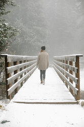 A woman walking on a footbridge in the mountains in snow. - MINF03529