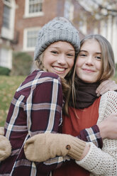 Two girls in hats and gloves wrapped up for cold weather, hugging and laughing. - MINF03532