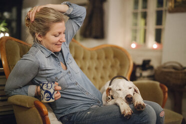 Eine Frau sitzt auf einem Sofa mit einem großen Hund, der seinen Kopf auf ihrem Schoß hat. - MINF03536