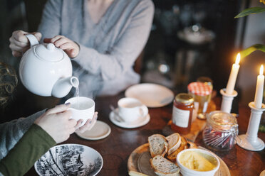 Eine Frau gießt Tee aus einer Teekanne in eine Tasse für einen Begleiter. - MINF03538