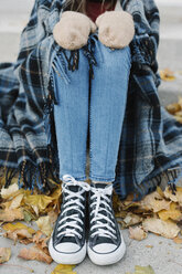 A young person sitting on a step with a warm plaid shawl around her. - MINF03540