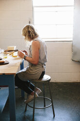 Eine Frau sitzt auf einem Hocker in einer Werkstatt. - MINF03545