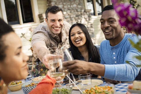 Freunde sitzen an einem Tisch, Männer und Frauen lachen und stoßen mit Weingläsern an. - MINF03556