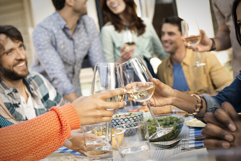 Freunde sitzen an einem Tisch, Männer und Frauen lachen und stoßen mit Weingläsern an. - MINF03559