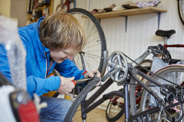 Ein junger Mann arbeitet in einer Fahrradwerkstatt und repariert ein Fahrrad. - MINF03605