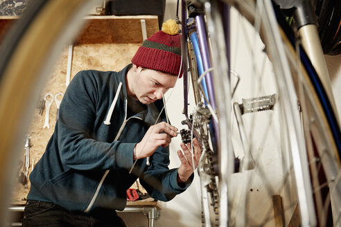Ein junger Mann arbeitet in einer Fahrradwerkstatt und repariert ein Fahrrad. - MINF03606