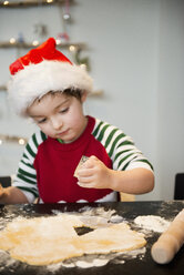 Ein Junge mit einer Weihnachtsmannmütze backt Weihnachtsplätzchen und schneidet Formen aus. - MINF03618