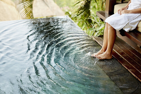 A person sitting on a bench with her feet in the shallow water of a pool, making ripples. - MINF03625