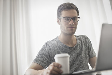 A working day. A man seated at a laptop computer, working in a hotel bedroom with a cup of coffee. - MINF03633