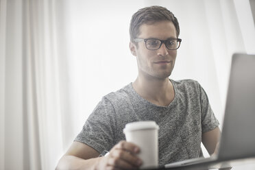 Ein Arbeitstag: Ein Mann sitzt an einem Laptop und arbeitet in einem Hotelzimmer mit einer Tasse Kaffee. - MINF03633