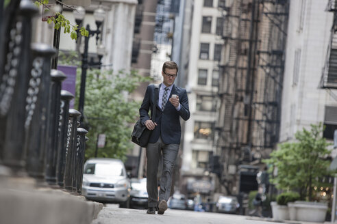 Ein Arbeitstag: Geschäftsmann in Anzug und Krawatte auf einer Straße in der Stadt, der sein Smartphone überprüft. - MINF03638