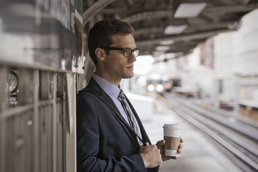 Ein Arbeitstag: Geschäftsmann in Arbeitsanzug und Krawatte mit einer Tasse Kaffee auf einem Bahnsteig. - MINF03639