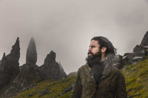 Ein Mann steht vor einer Kulisse aus Felszacken am Horizont, einer dramatischen, windgepeitschten Landschaft und tief hängenden Wolken. - MINF03659