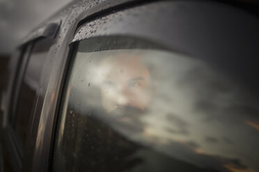 A man sitting in a car looking out. Reflections of the sunset sky on the window. - MINF03666