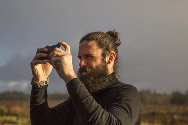 Ein Mann steht mit seinem Smartphone vor einem grauen Himmel und macht ein Foto. - MINF03670