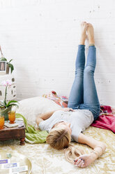 A young woman in jeans lying on her back with her legs against the wall. - MINF03677