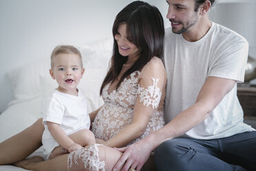 Ein junges Paar und sein kleiner Sohn sitzen zusammen auf ihrem Bett. - MINF03699