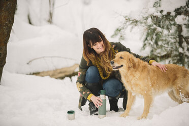 Eine Frau streichelt einen Golden Retriever in einem winterlichen Waldgebiet. - MINF03730