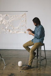 An artist working on an art piece, creating a woven and stitched object with thread. - MINF03737