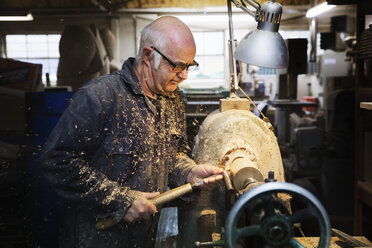 Ein Mann steht an einer Holzbearbeitungsmaschine in einer Schreinerei und dreht ein Stück Holz. - MINF03748