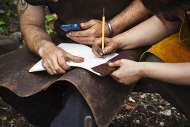 Two men wearing aprons writing into a notebook sat in a garden. - MINF03770