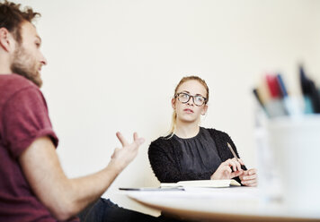 Zwei Personen in einer Besprechung, ein Mann, der gestikuliert, und eine Frau, die zuhört. - MINF03776