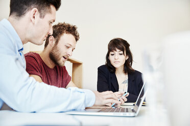 Three people seated at a table at a business meeting using and sharing a laptop screen. - MINF03779