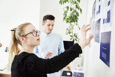 Two people looking at printed plans stuck on a wall, project management and discussions. - MINF03780