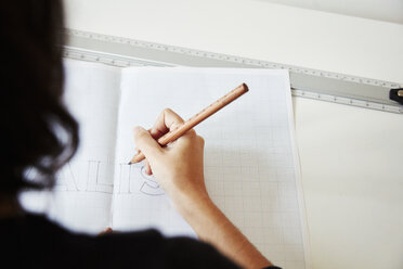 Over the shoulder view of a woman working on a graphic on a drawing board, outlining letters with a pencil. - MINF03784