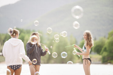 Teenage girls standing by a lake, surrounded by soap bubbles. - MINF03805