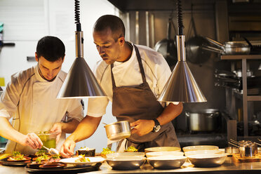 Two chefs standing in a restaurant kitchen, plating food. - MINF03816