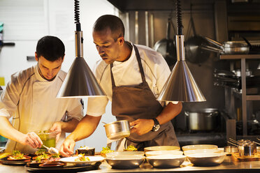 Zwei Köche stehen in einer Restaurantküche und richten das Essen an. - MINF03816