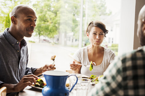Zwei Männer und eine Frau sitzen an einem Tisch in einem Café und essen zu Mittag. - MINF03843