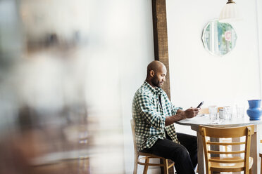 Man wearing a checked shirt sitting in a cafe, using his mobile phone. - MINF03846