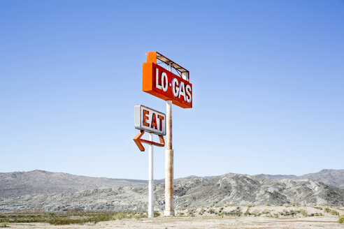 Large red and silver sign on metal poles advertising petrol station and diner , mountains in the distance. - MINF03912