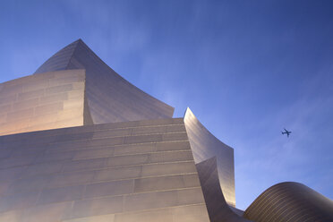 Niedriger Blickwinkel auf ein modernes Gebäude mit Blechfassade von Frank Gehry, Passagierflugzeug fliegt vorbei. - MINF03925